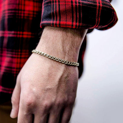 Hand wearing a gold chain bracelet with a red plaid shirt sleeve.
