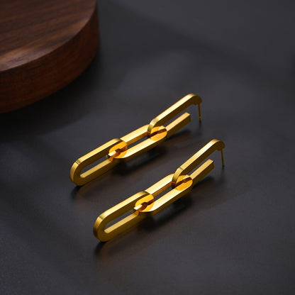 Gold chain-style earrings on a dark surface with a wooden object in the background
