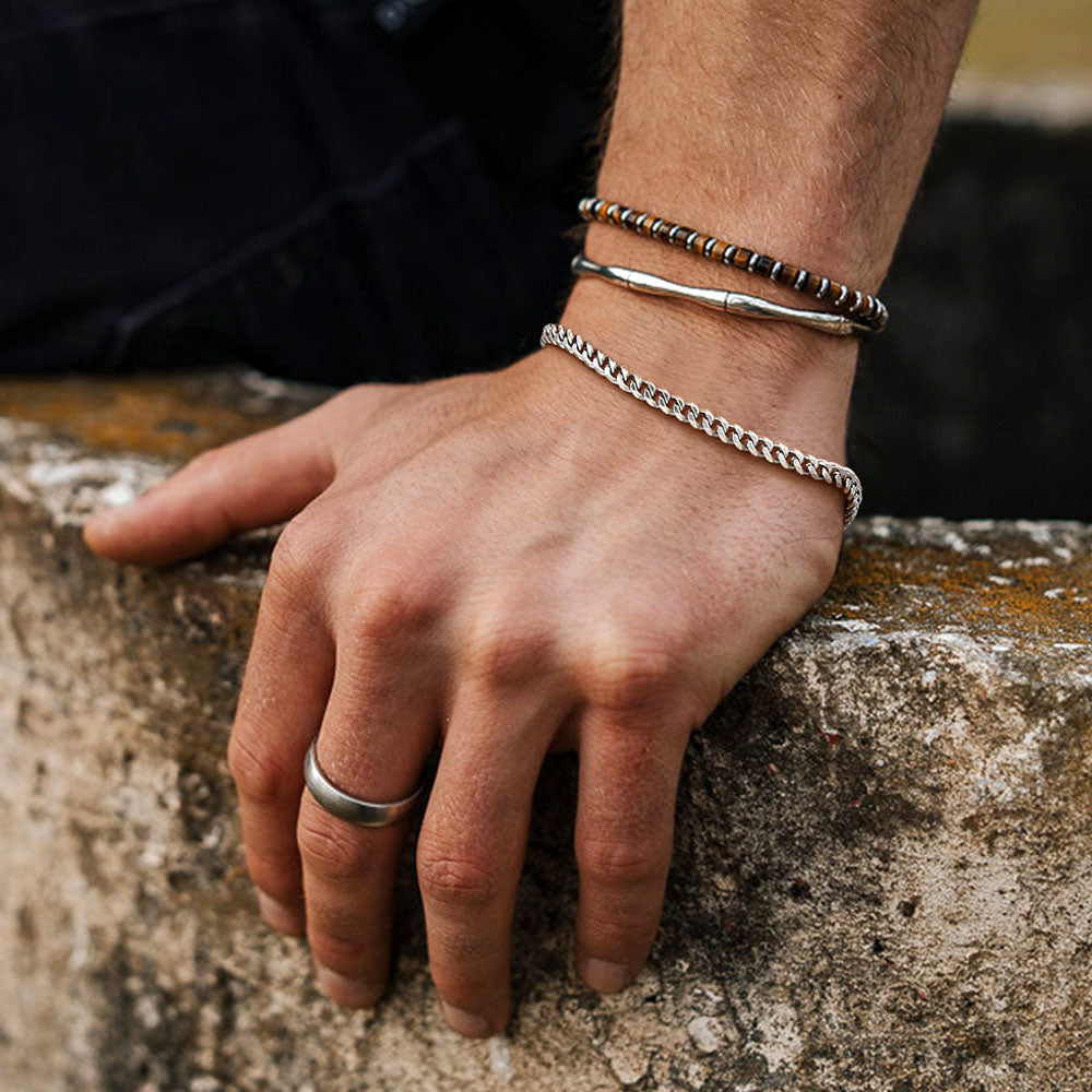 Hand wearing multiple silver bracelets on a stone surface