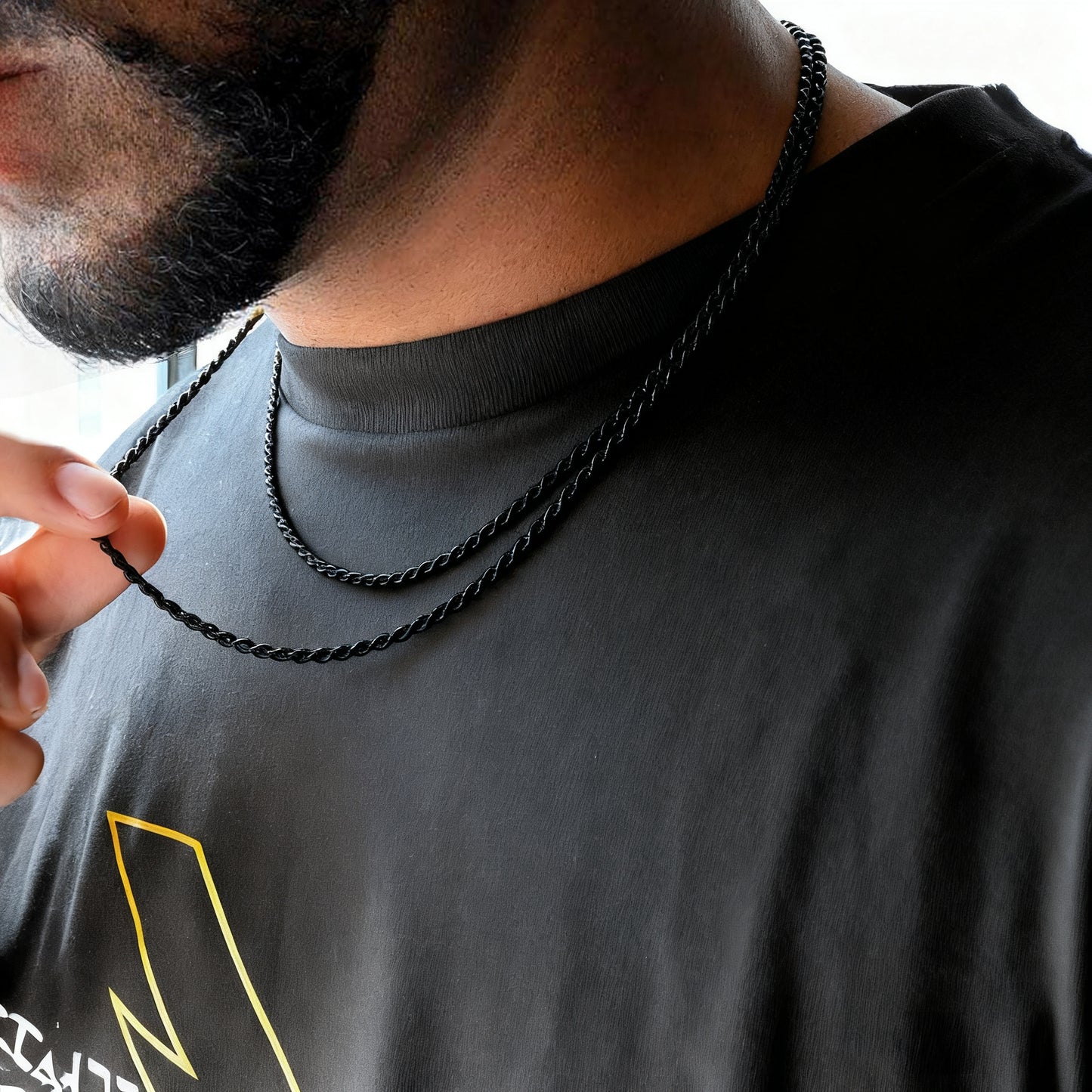 Person wearing a black rope chain necklace with a blurred background