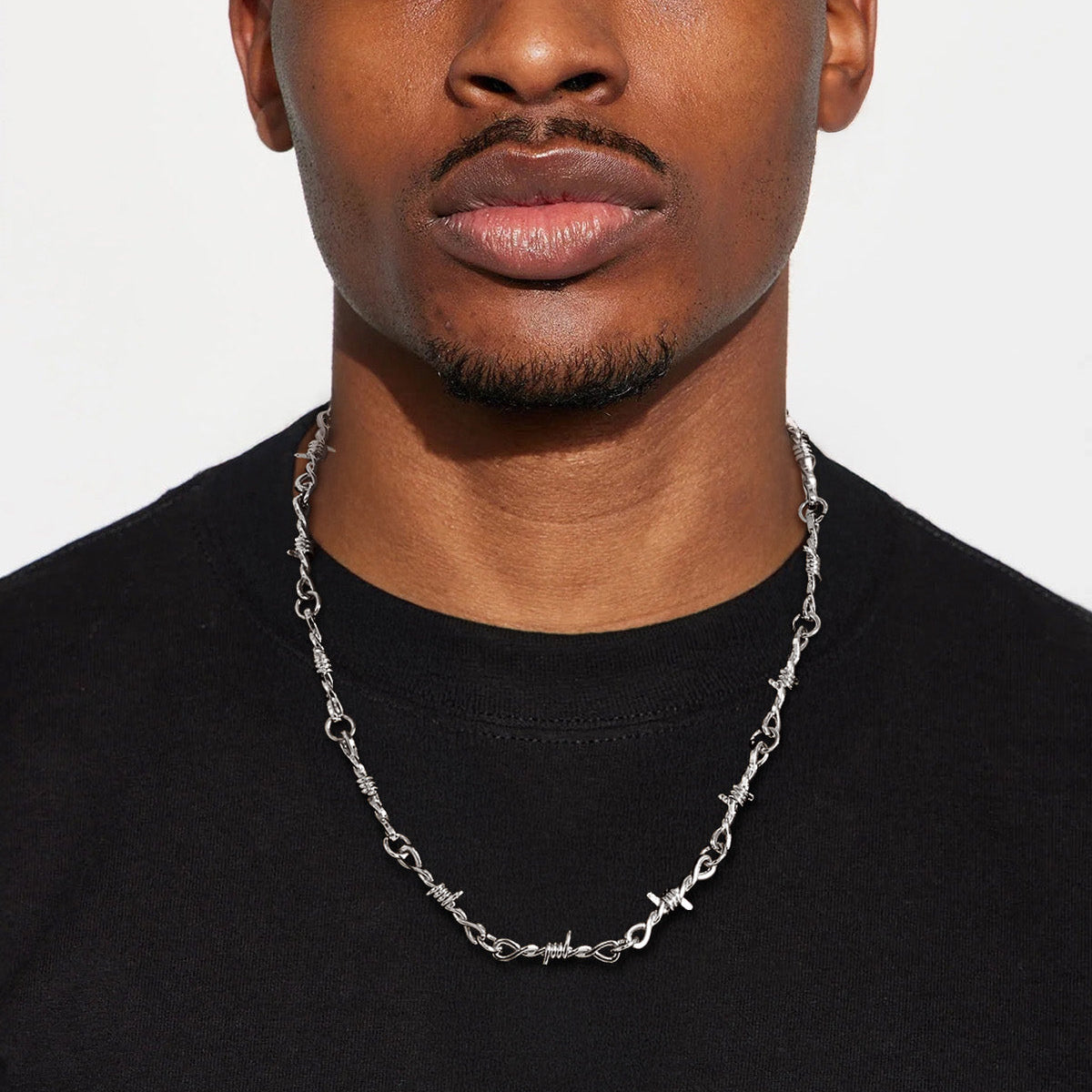 Man wearing a black shirt and chain necklace against a white backgroundimg