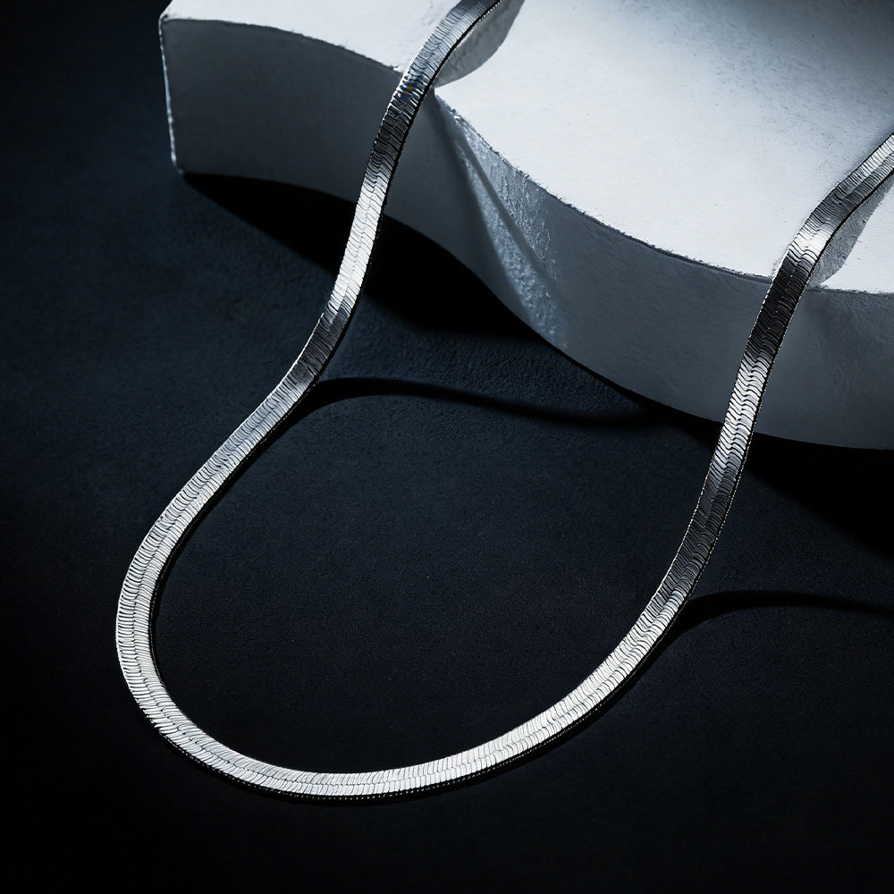 Silver necklace on a dark surface with a white fabric background