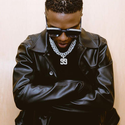 Person wearing a black leather jacket, sunglasses, and a chain necklace with a number '99' pendant.