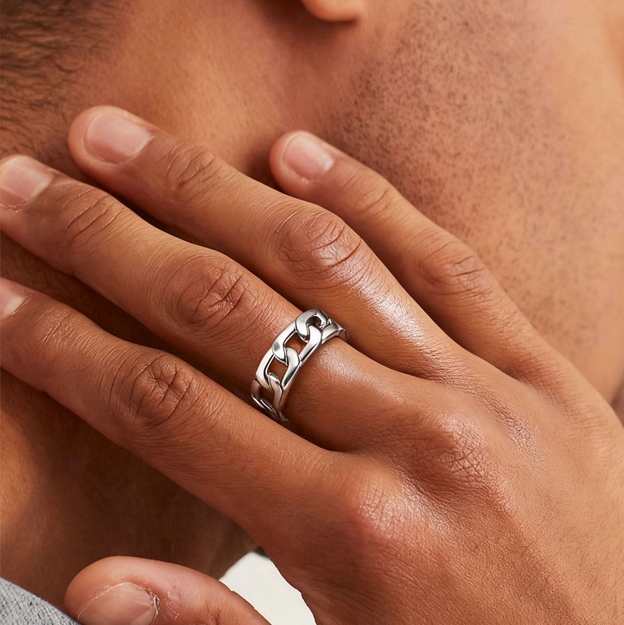 Close-up of a hand wearing a silver chain ring with a neutral background