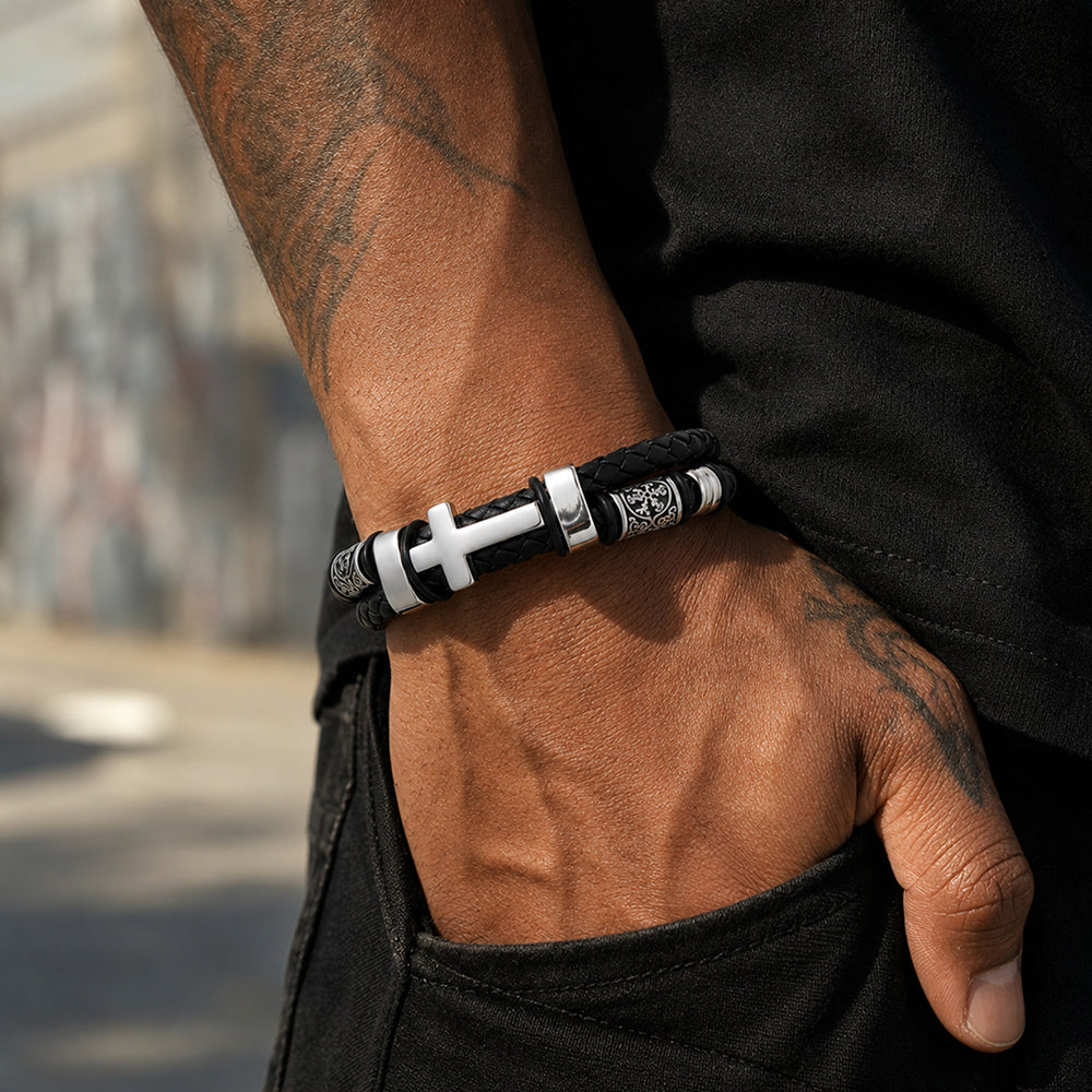 A close-up of a person wearing a black and silver beaded bracelet with a cross charm