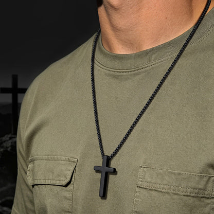 Person wearing a green shirt with a black cross necklace against a dark background