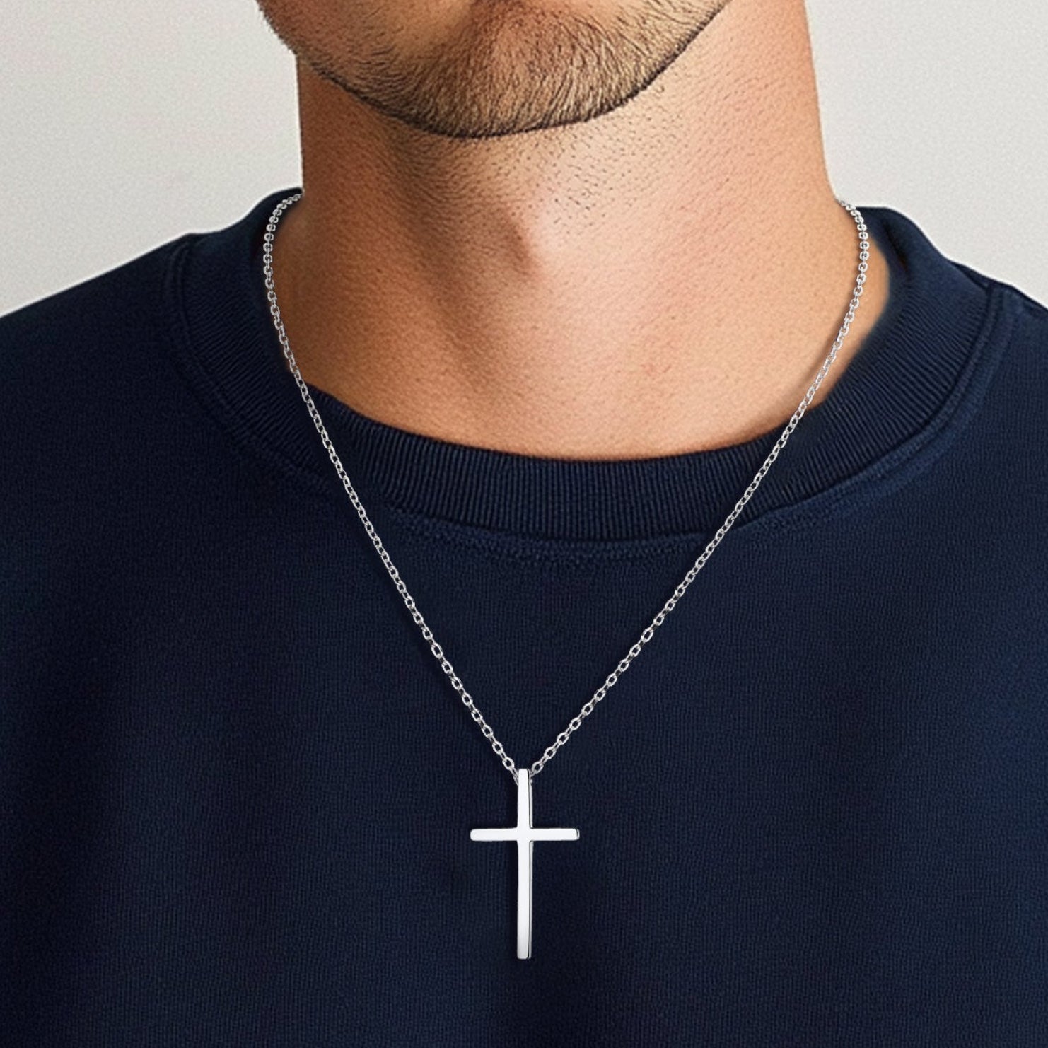 Man wearing a navy blue sweatshirt with a silver cross necklace on a plain background