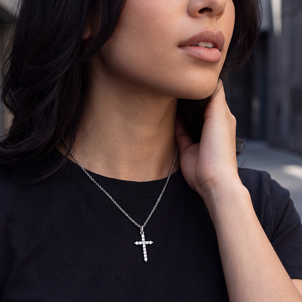 A close-up of a woman wearing a silver cross pendant necklace with clear stones.