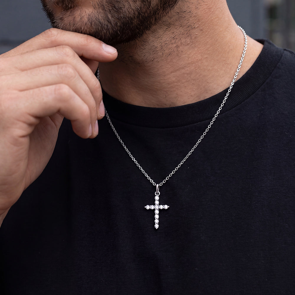 A man wearing a silver cross pendant necklace adorned with small clear stones.