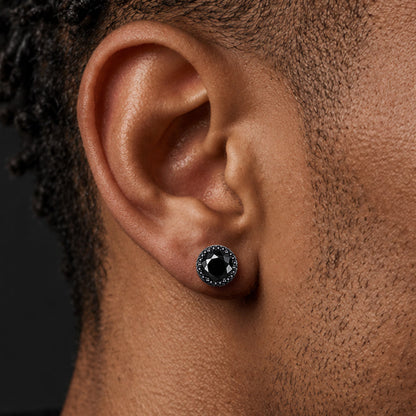 A man's ear wearing a small round stud earring with a black center and a halo of tiny clear stones.