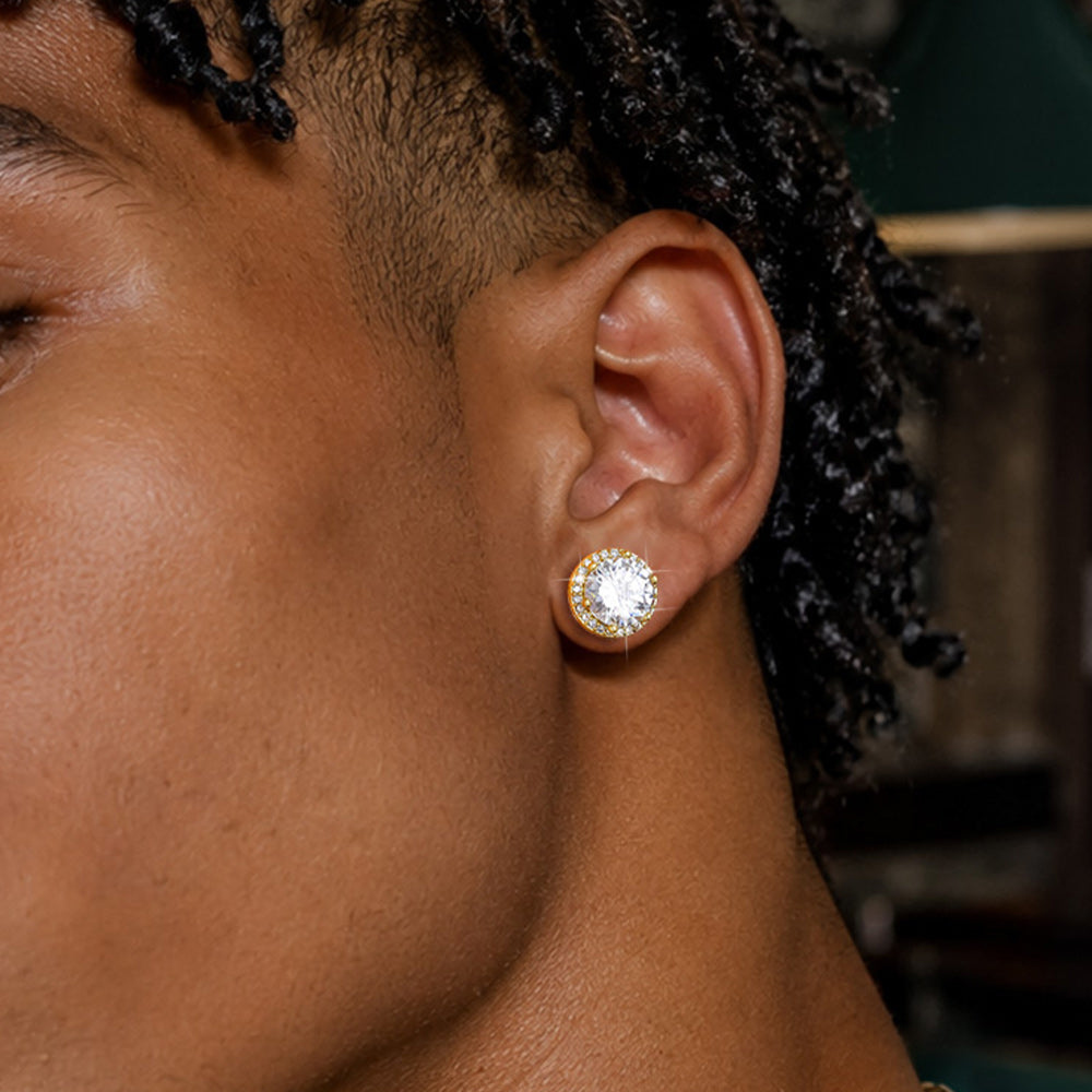 A person wearing a gold stud earring with a clear round gemstone.