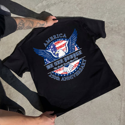 Black t-shirt with a patriotic design featuring an eagle and text, held by a person on a concrete surface.