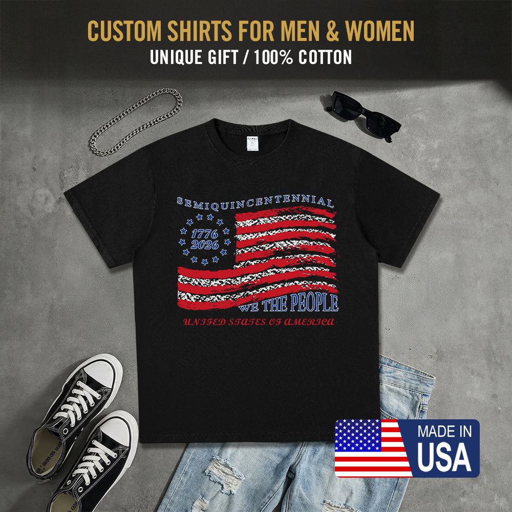 Black t-shirt with American flag design, sunglasses, sneakers, and jeans on a gray surface.