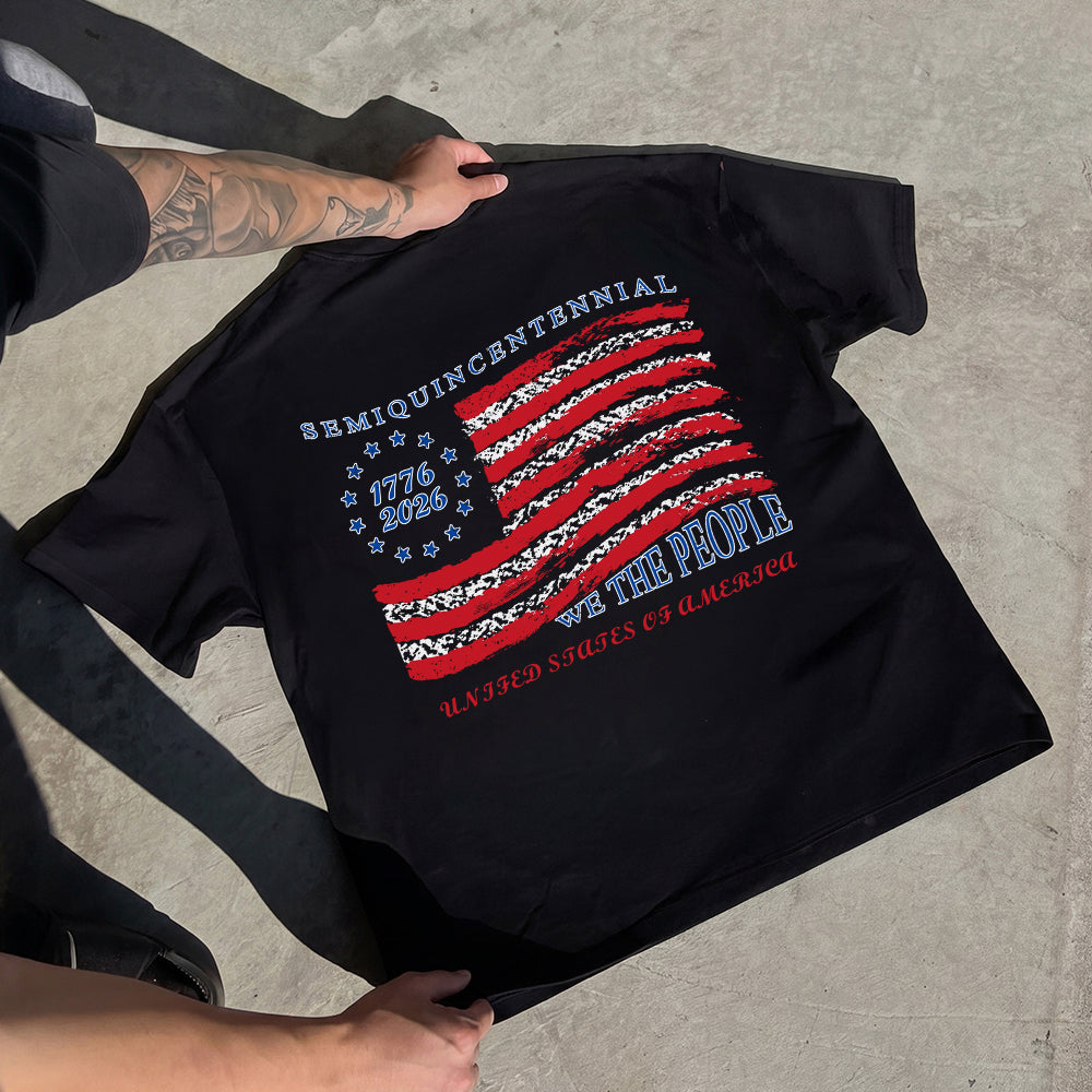 Black t-shirt with American flag design and text held by a person on a concrete surface