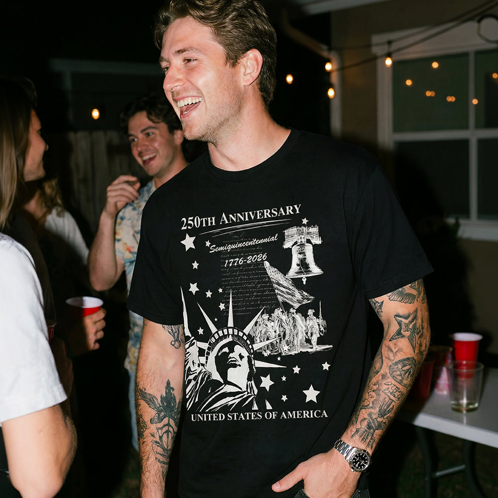 Man wearing a black t-shirt with a 250th Anniversary design, standing in a social setting.