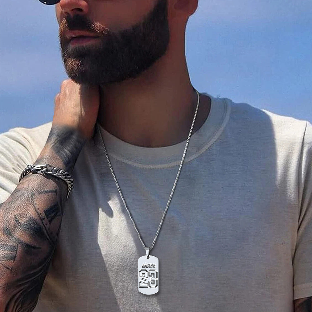 A man wearing a silver chain necklace with a rectangular dog tag pendant.