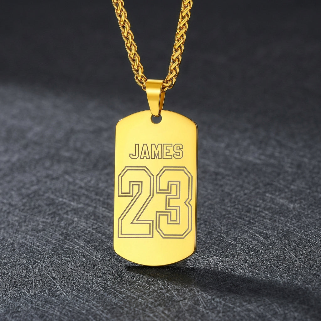A gold-plated dog tag necklace engraved with the name and the number on a drak  background.