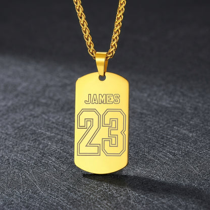 A gold-plated dog tag necklace engraved with the name and the number on a drak  background.