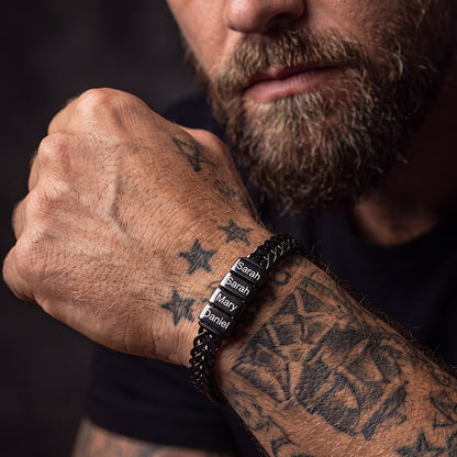 A close-up lifestyle shot of a man's wrist wearing a black custom name chain bracelet.
