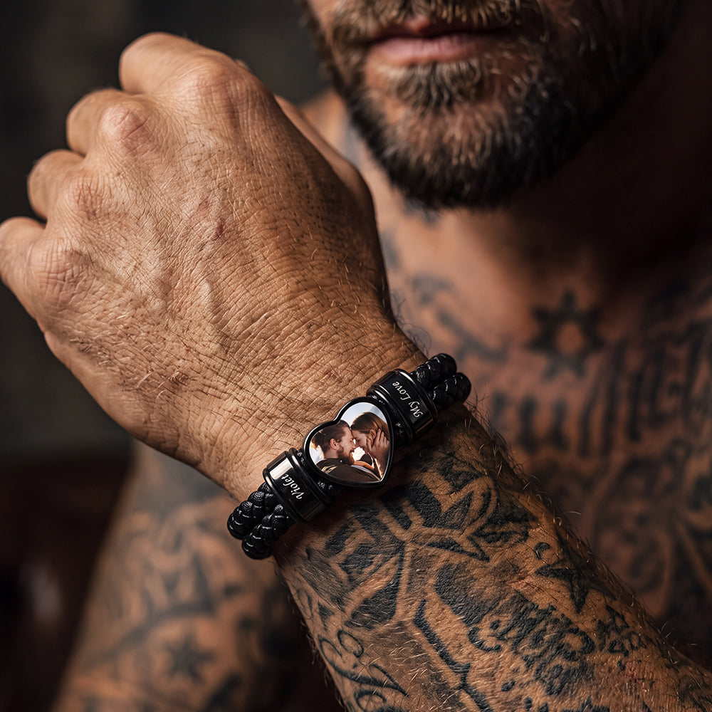 A man wearing a black braided bracelet with a polished heart-shaped centerpiece that reflects his face.