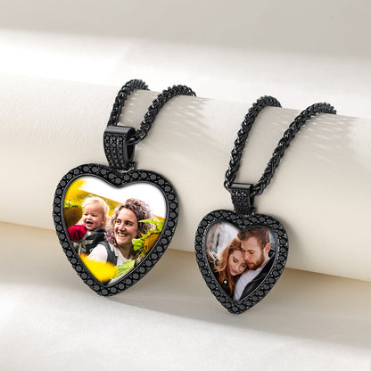 Two black CZ heart-shaped photo pendant necklaces displayed on a white cylindrical stand against a light beige background. 