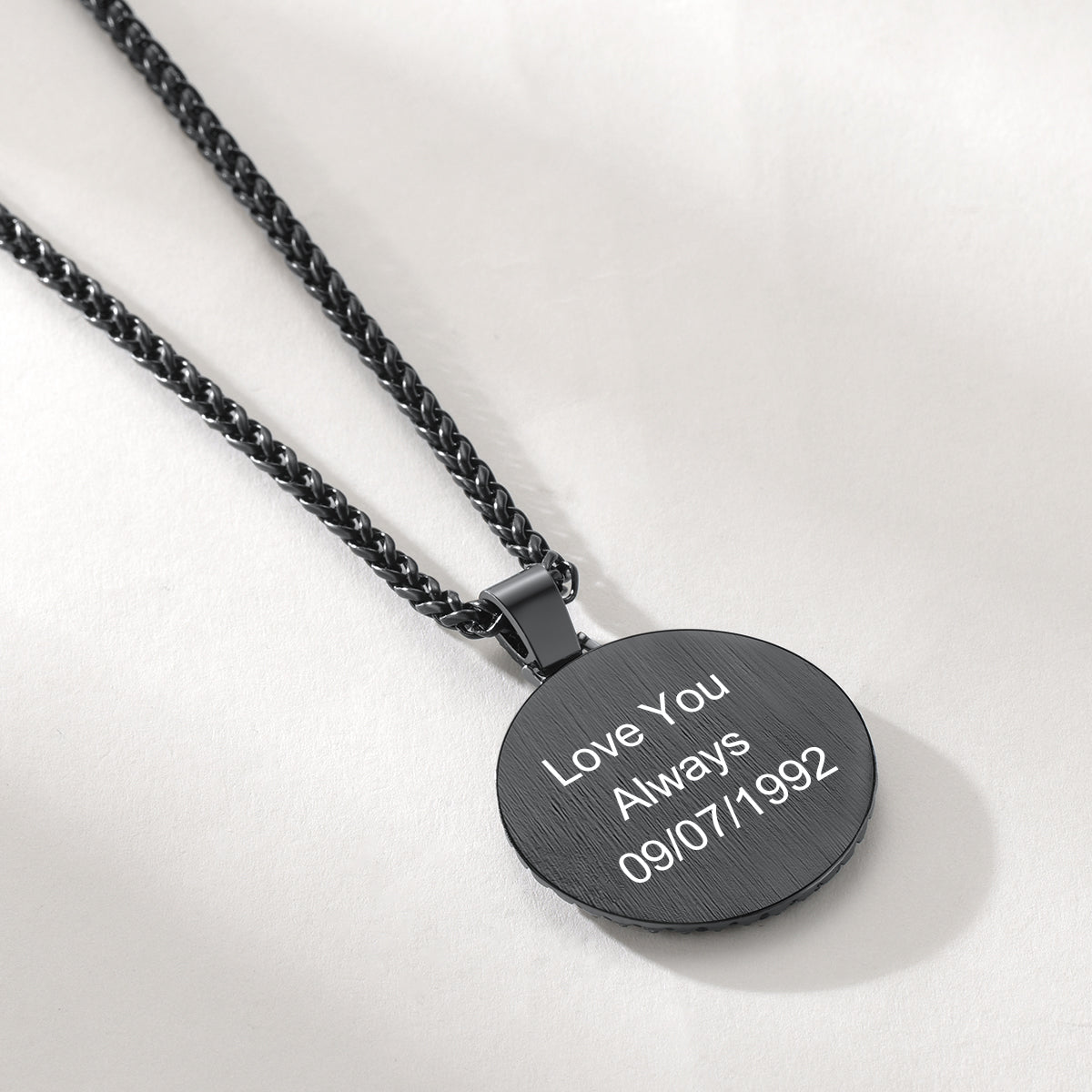 A black round pendant necklace engraved with 'Love You Always 09/07/1992'.background.