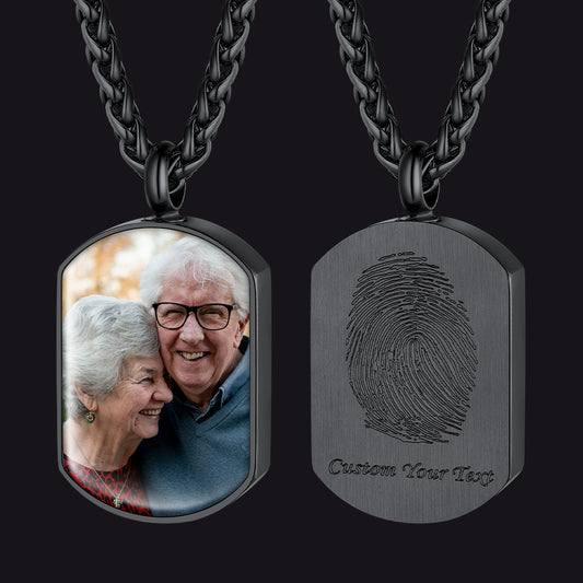Two views of a black metal dog tag necklace on a black background. The left pendant shows a custom photo of an elderly couple, while the right pendant shows a brushed black finish with an engraved fingerprint and the text 'Custom Your Tags'.img