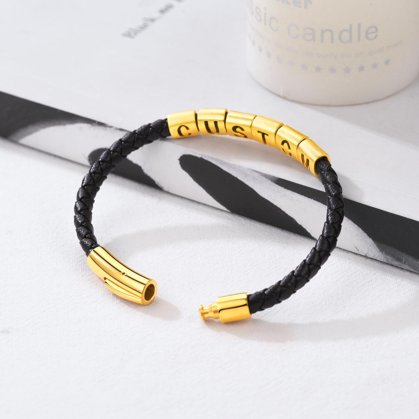 Black braided bracelet with gold cylindrical beads on a white surface