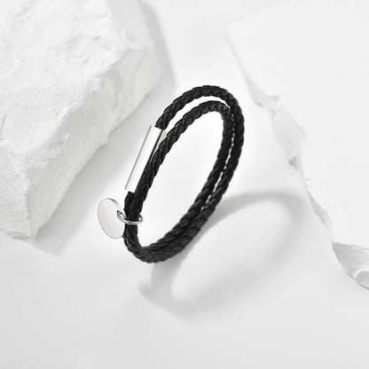 Black braided bracelet with silver tag on a white fabric background