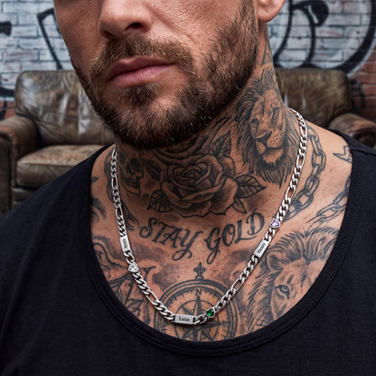 A close-up of a man wearing a silver chain necklace with engraved nameplates and gemstone.