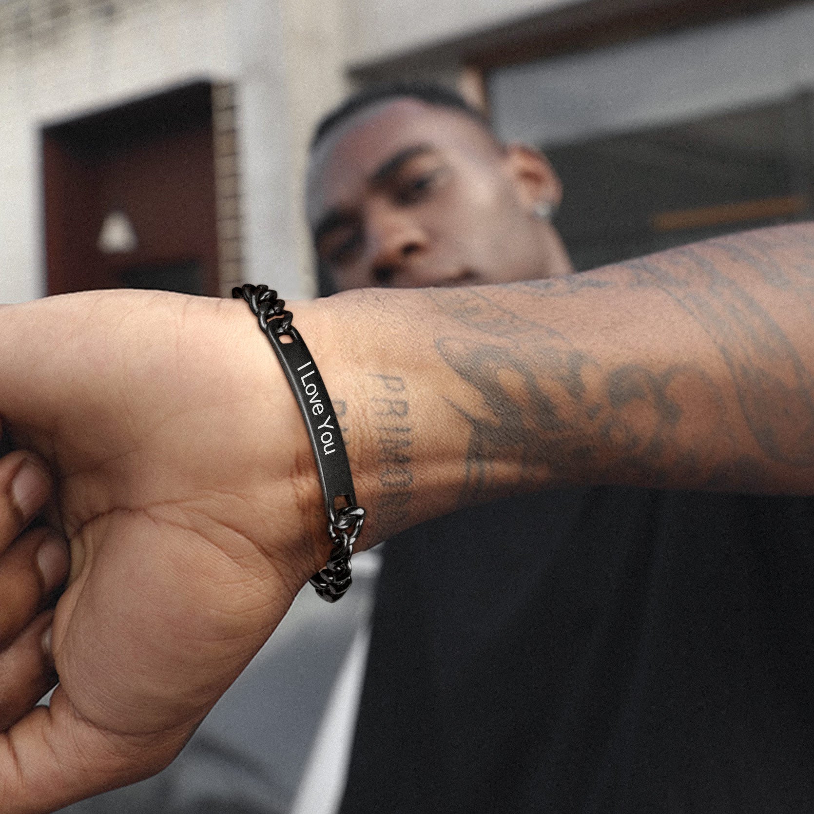 Person wearing a black bracelet with 'I Love You' on a blurred background