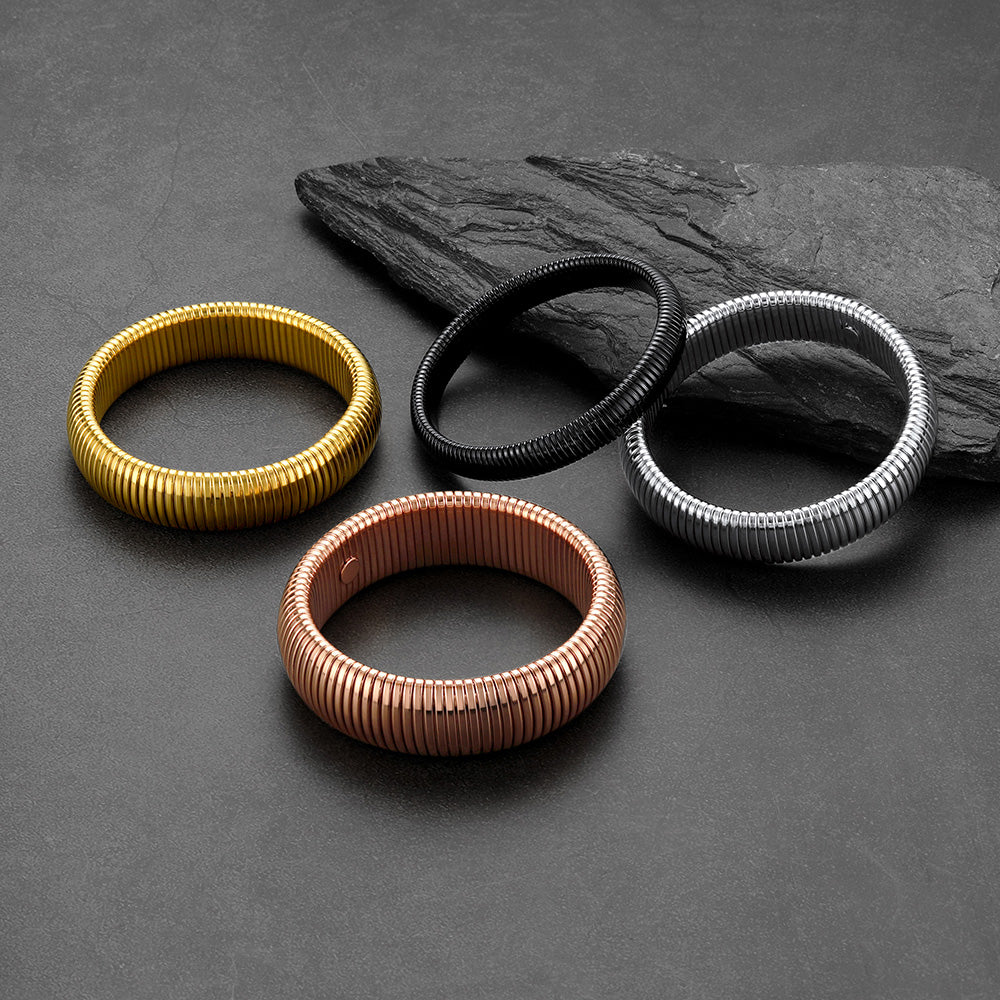 Four metallic bracelets in gold, black, rose gold, and silver on a dark stone surface.