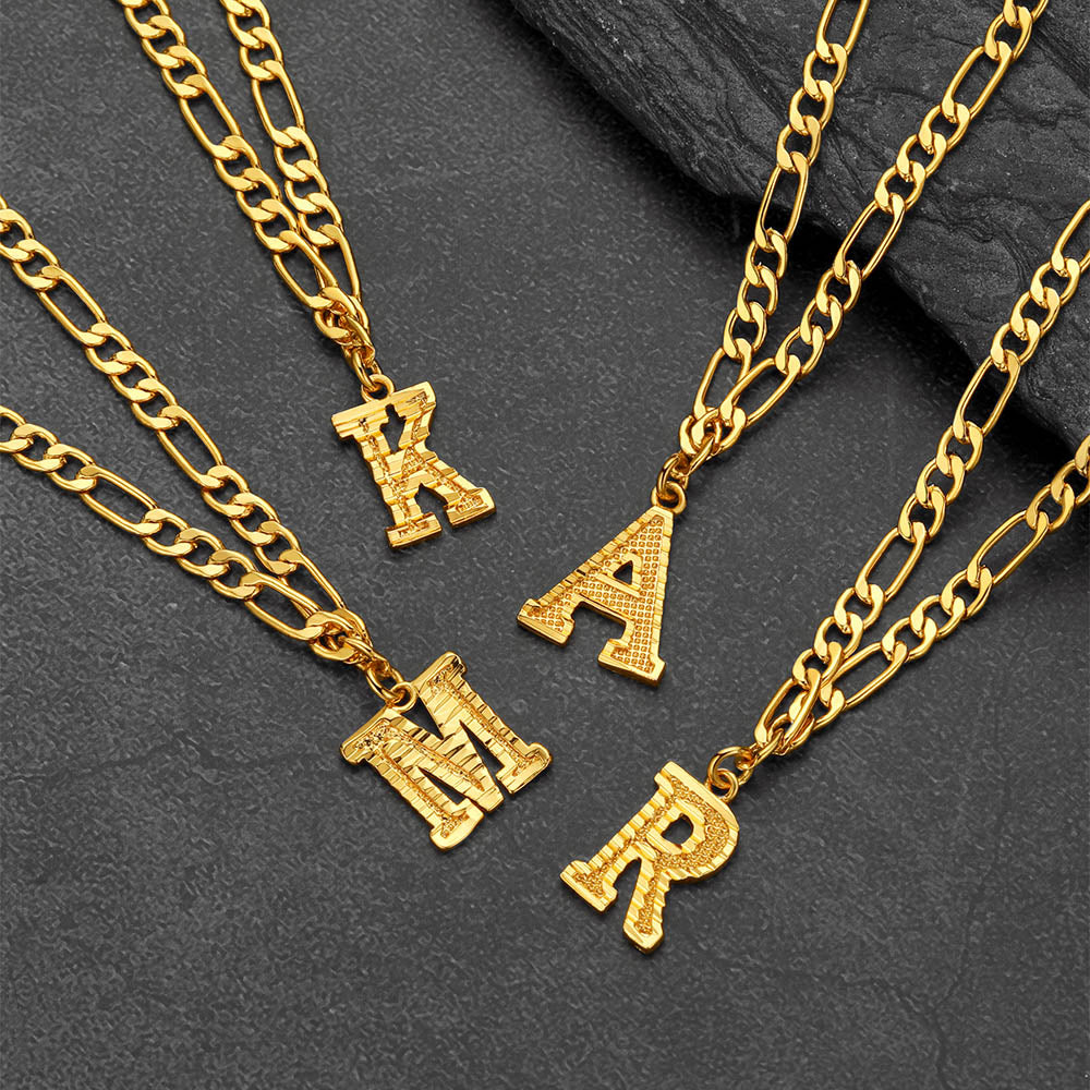 Gold chain necklaces with letter pendants on a dark stone surface