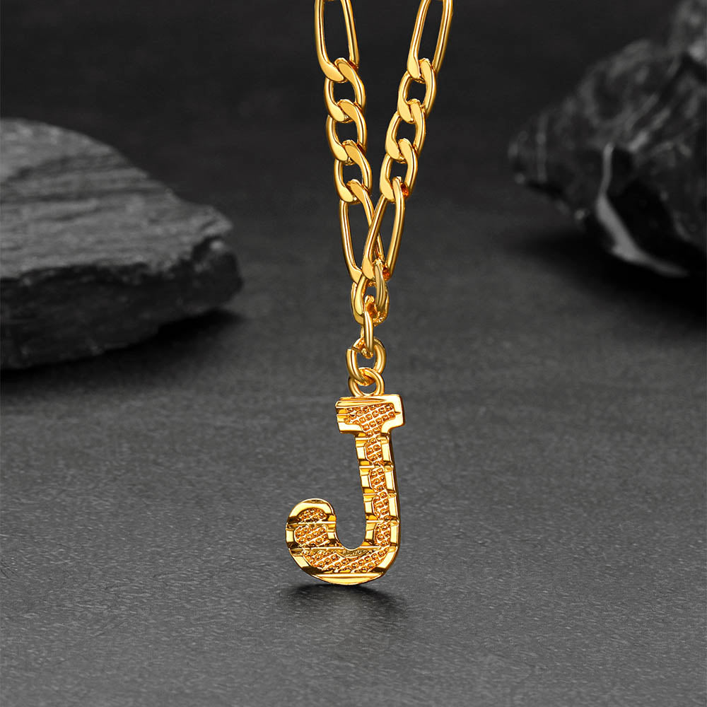 Gold necklace with a 'J' pendant on a dark surface