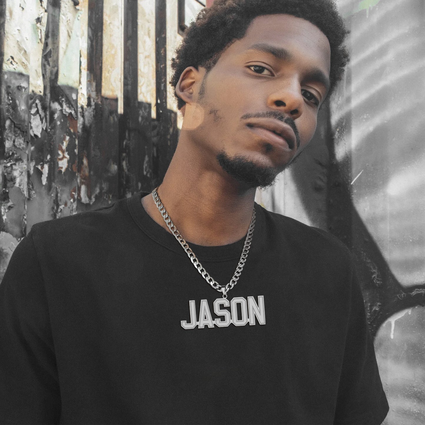 Man wearing a black shirt with 'JASON' Initial Letter Necklace on it, standing against a textured wall.