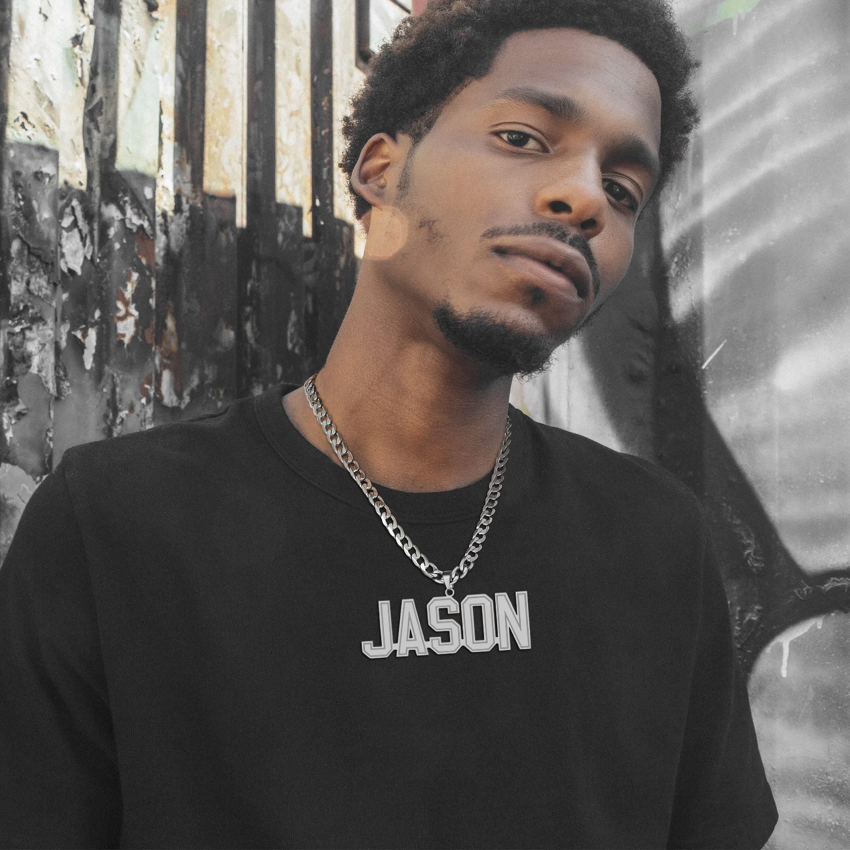 Man wearing a black shirt with 'JASON' Initial Letter Necklace on it, standing against a textured wall.