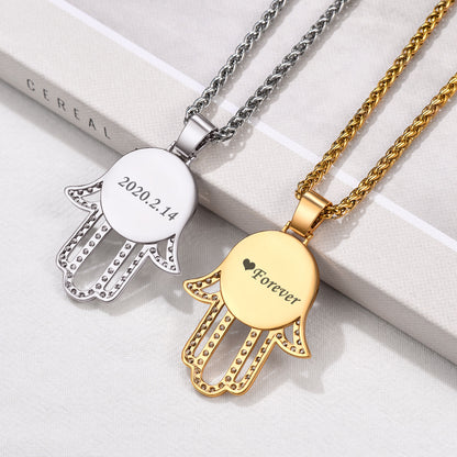 Two Hamsa hand pendants, one silver and one gold, on a white surface.