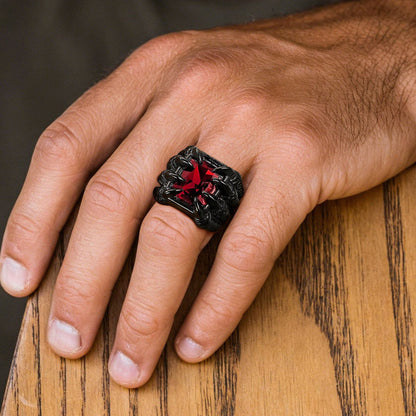 A close-up of a man's hand resting on a wooden table, wearing a chunky black ring with a red star design in the center.