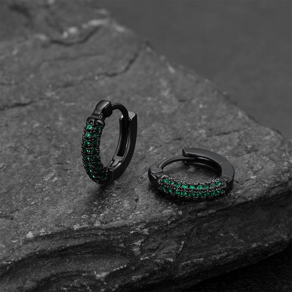 Black hoop earrings with green gemstones on a dark stone surface