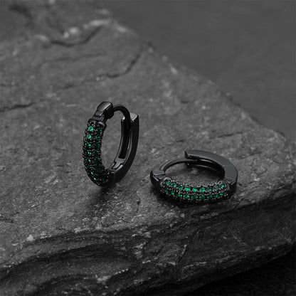 Black hoop earrings with green gemstones on a dark stone surface