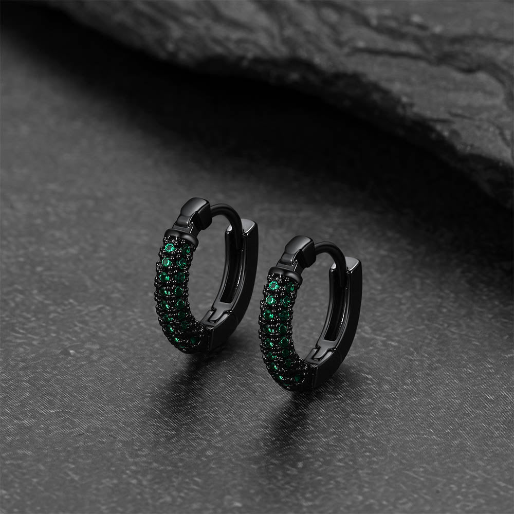 Black hoop earrings with green gemstones on a dark textured surface