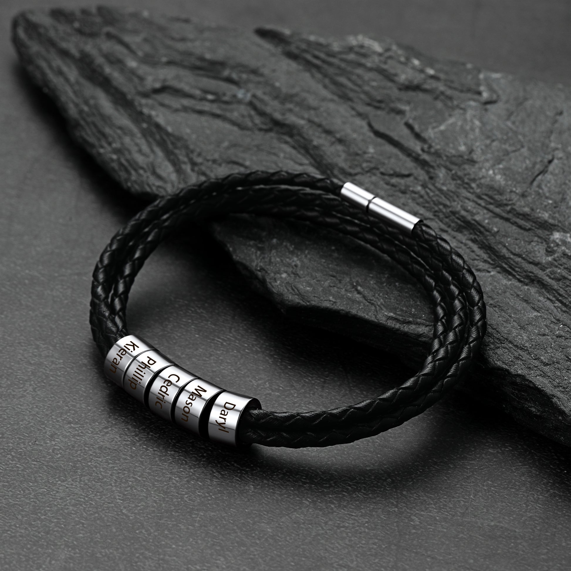 Black braided leather bracelet with metal tags on a dark stone surface