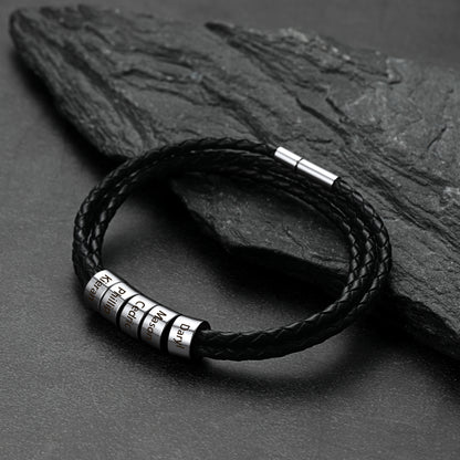 Black braided leather bracelet with metal tags on a dark stone surface