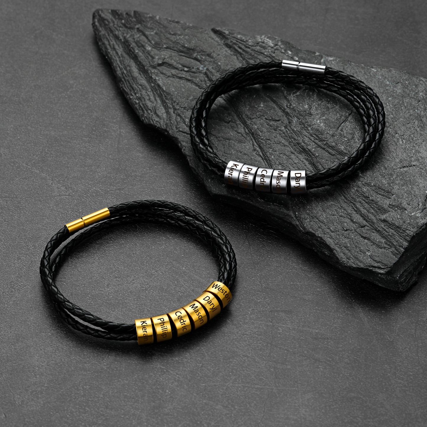 Two black leather bracelets with metal beads on a dark stone surface