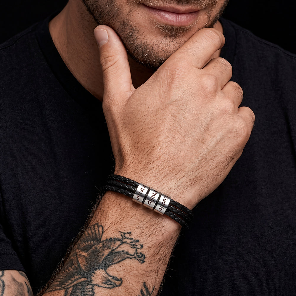 Man wearing a black leather bracelet with metal beads on his wrist, against a dark background.