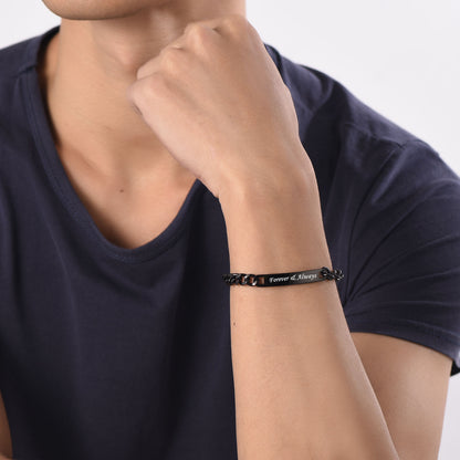 Person wearing a black bracelet with 'Forever & Always' on a plain background