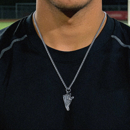 Person wearing a black shirt with a necklace, standing in front of a sports field at night.