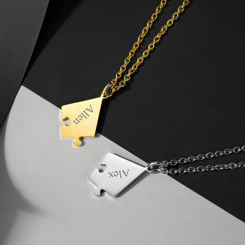 Two gold and silver puzzle piece pendants on chains against a black and gray background.