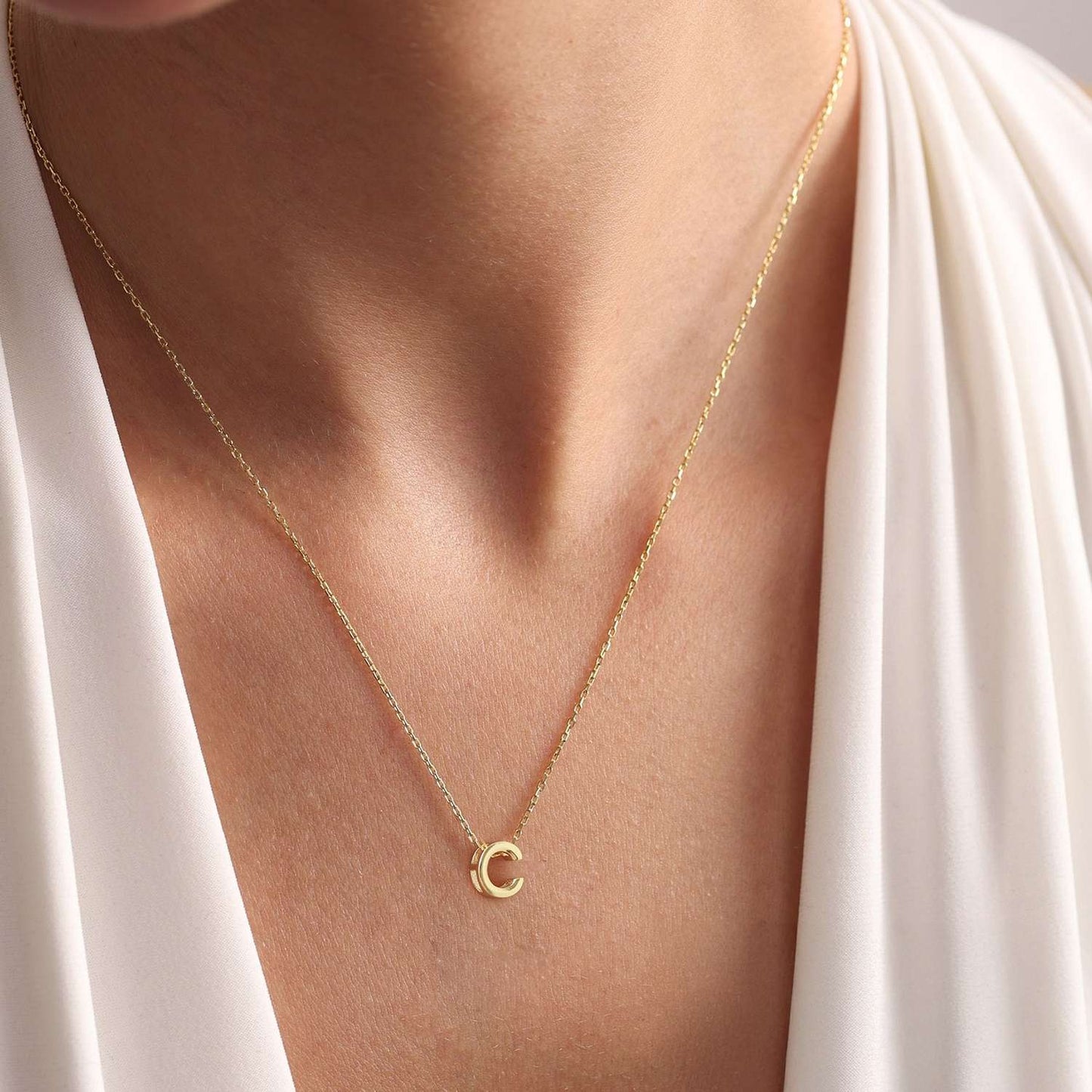 Gold initial necklace with a small pendant on a person
