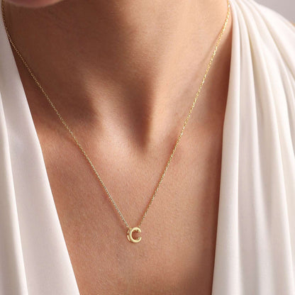 Gold initial necklace with a small pendant on a person
